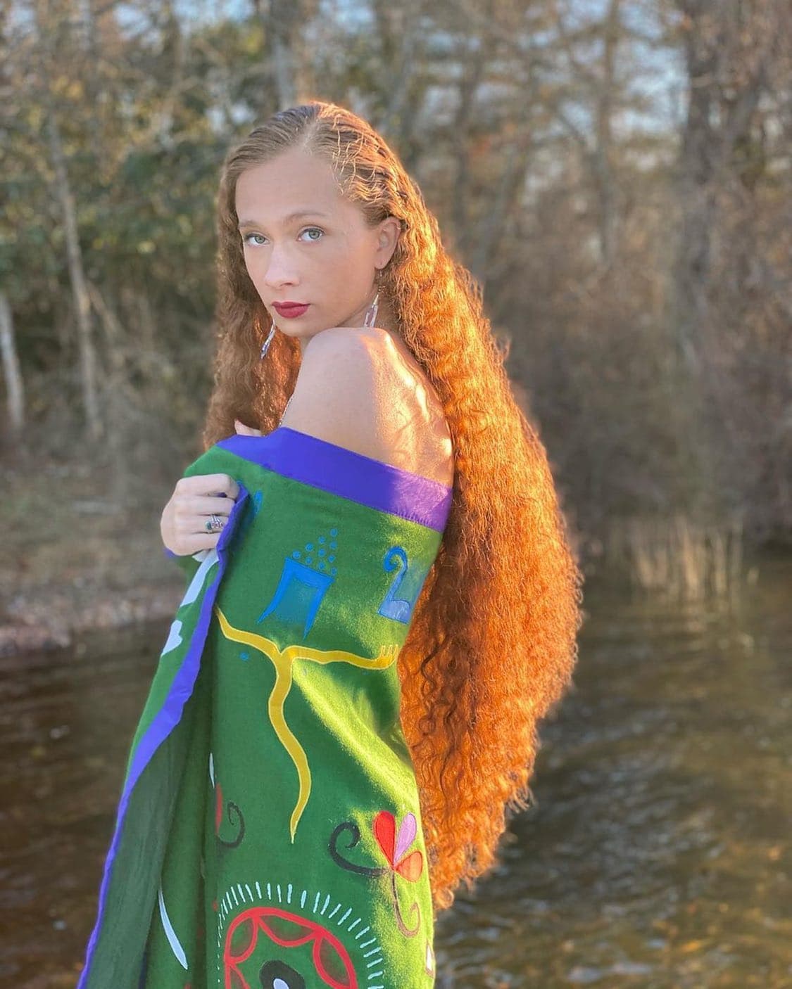 A person with long hair stands with a green and blue blanket wrapped around them.